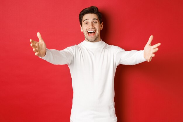Image of happy friendly man in white sweater reaching hands and smiling while greeting guests to chr...