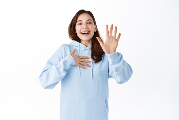 Image of happy friendly woman say her name introduce herself pointing at chest and raising hand volunteering wants to participate standing over white background