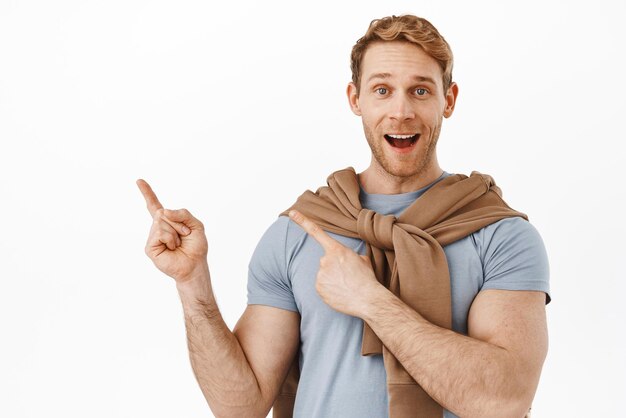 Image of happy ginger guy with fit and sporty body say wow smiling excited and pointing at upper left corner showing announcement recommending product point at logo white background