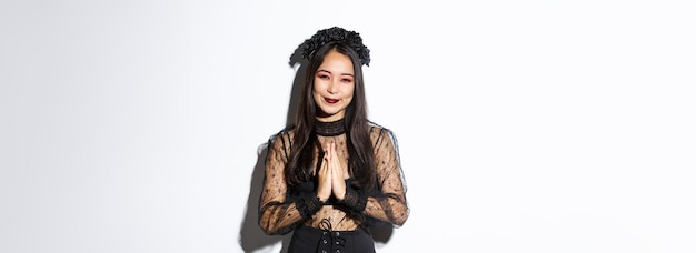 Free photo image of happy and grateful young asian woman in gothic lace dress clasp hands together to say thank