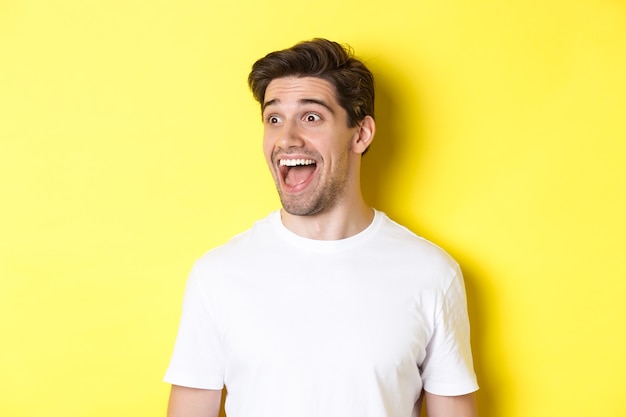 Image of happy man checking out promo, looking left with amazement, standing in white t-shirt against yellow background