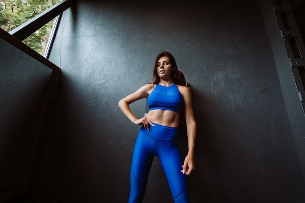 Image of happy sports young girl standing and posing over black wall. Looking at camera. Female resting after fitness.