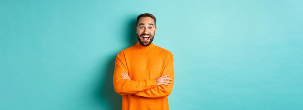 Image of happy and surprised man reacting to news looking amazed standing in orange sweater against