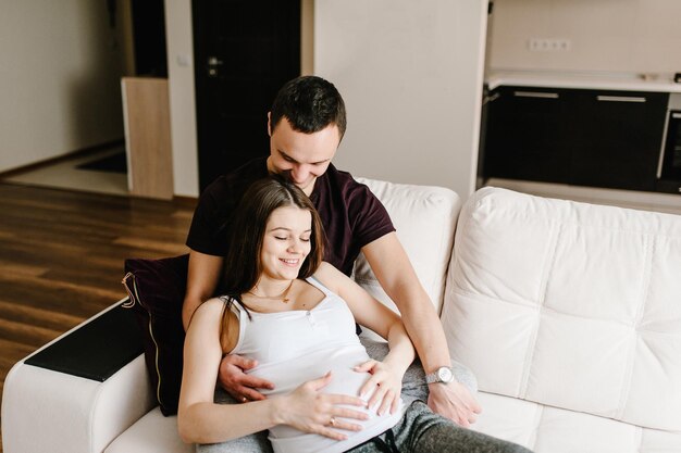 Image of husband holding belly of his pregnant wife making symbol heart hands. pregnant woman and loving handsome man hugging tummy at home. loving couple. parenthood concept. baby shower.