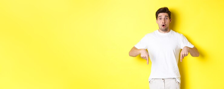 Free Photo image of impressed guy pointing fingers down gasping amazed and looking at camera standing over yell
