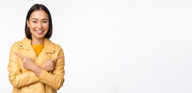 Free photo image of indecisive asian girl pointing fingers sideways pointing left and right choosing variant deciding standing over white background