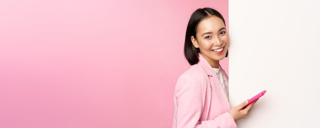 Image of korean female entrepreneur in suit standing near info wall advertisement on board holding s