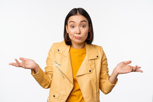 Image of korean girl shrugs shoulders and looks confused dont know cant tell standing over puzzled over white background