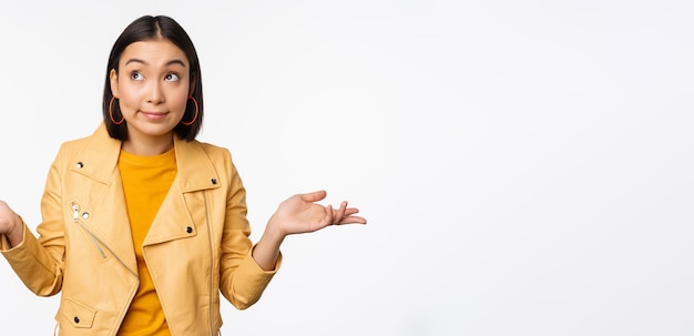 Image of korean girl shrugs shoulders and looks confused dont know cant tell standing over puzzled over white background