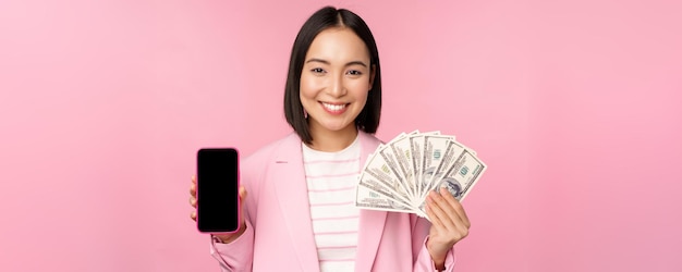 Immagine di una donna d'affari coreana di successo che mostra i dollari di denaro e l'interfaccia dello schermo dell'app per smartphone