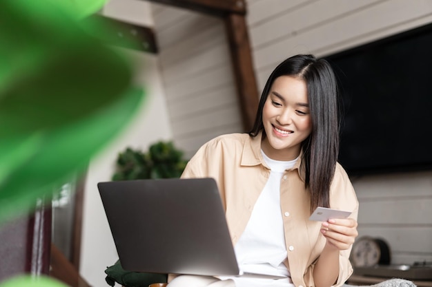 Image of korean woman buying smth online paying with credit card on website purchase on laptop from ...