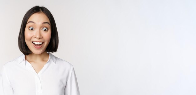 Image of korean woman looking surprised and happy at camera standing over white background