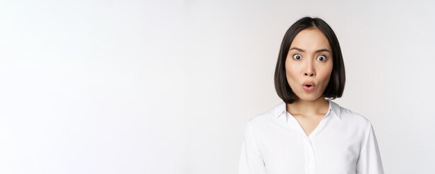 Image of korean woman looking surprised and happy at camera standing over white background