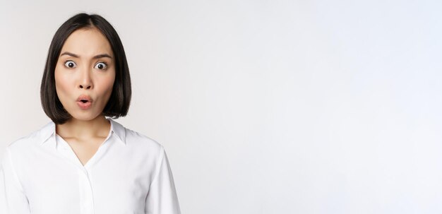 Image of korean woman looking surprised and happy at camera standing over white background