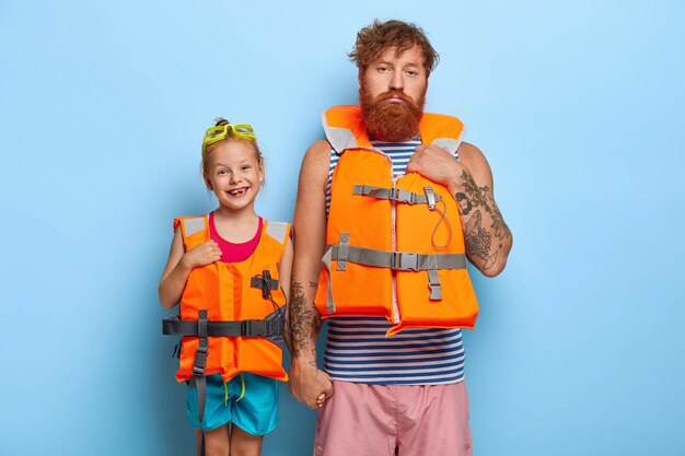 Image of lovely glad little girl wears swimming goggles and orange lifejacket