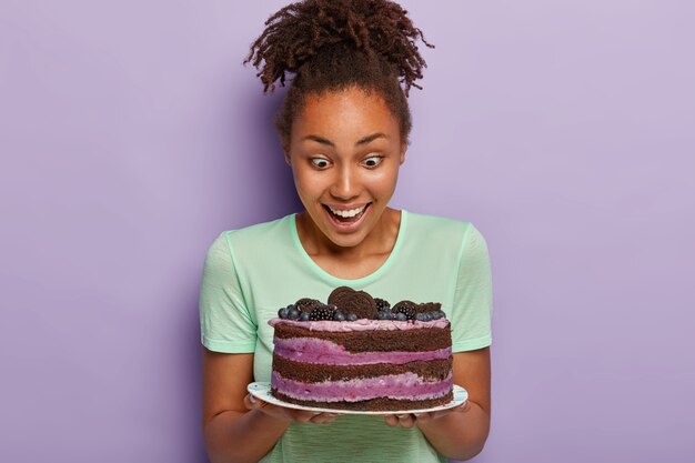 건강한 어두운 피부를 가진 사랑스러운 여자의 이미지, 접시에 맛있는 과일 케이크에서 행복을 쳐다 본다.