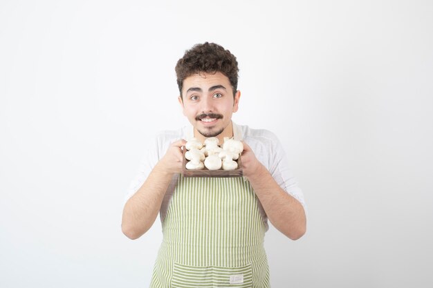 Image of male cook holding plate of raw mushrooms on white 