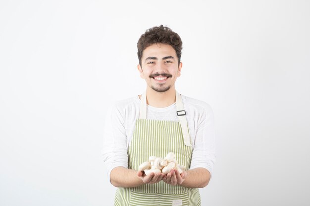 Изображение мужского повара, держащего сырые грибы с счастливым выражением лица на белом