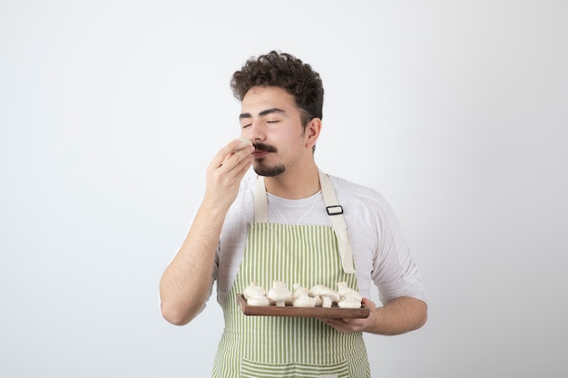 Image of male cook smells raw mushrooms on white 