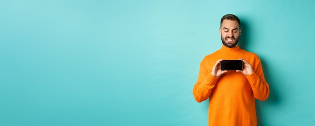 Free photo image of man cringe at something on mobile screen staring disgusted at display showing smartphone st