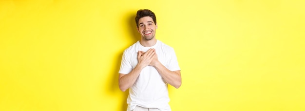 Бесплатное фото Изображение благодарного красивого парня в белой футболке, держащего руки на сердце и улыбающегося