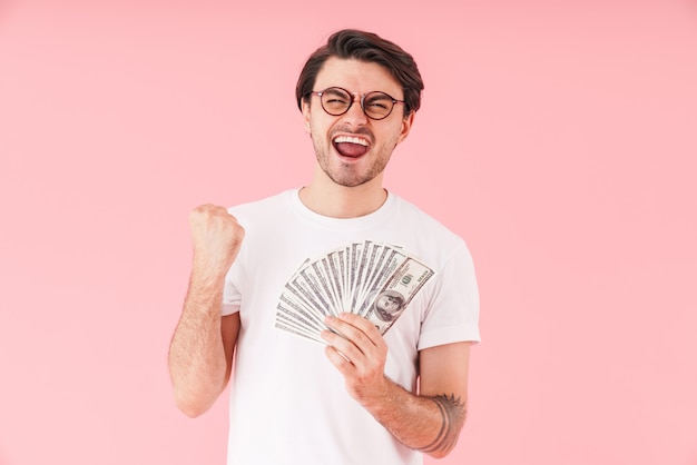 Изображение счастливого молодого человека в очках, держащего наличные деньги и показывающего жест победителя изолированы