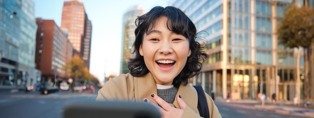 無料写真 スマートフォンでビデオチャットする韓国の女の子の画像は、驚いて驚いた顔で携帯電話を見ています