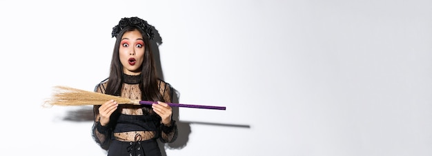 Бесплатное фото Изображение удивленной женщины в костюме на хэллоуин, держащей ведьмину метлу и изумленно смотрящей в камеру