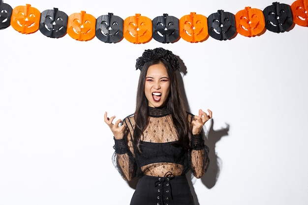 Бесплатное фото Изображение злой ведьмы, злой смеющейся и гримасничающей, женщины, празднующей хэллоуин на фоне праздничных украшений, стоящей над тыквенными лентами.