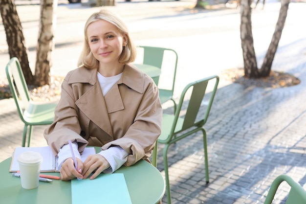無料写真 外のカフェでコーヒーを飲みながら書いている若い女性起業家のイメージ