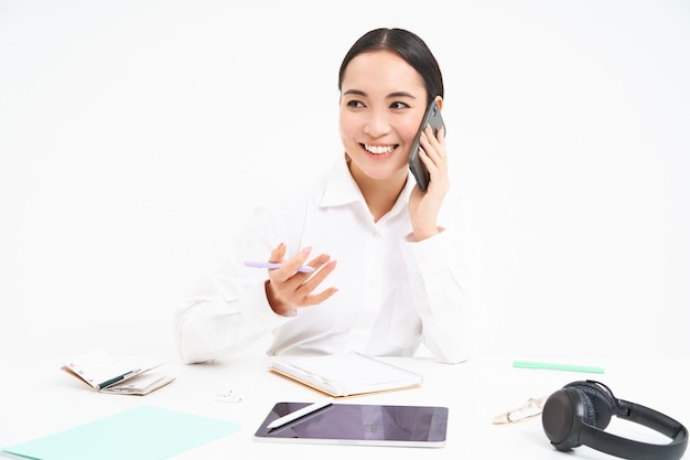 Free photo image of office employee asian woman in office talks on mobile phone discusses work on cellphone whi