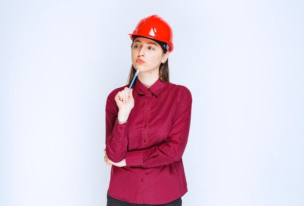 Image of pensive woman in crash helmet holding pencil and posing . 