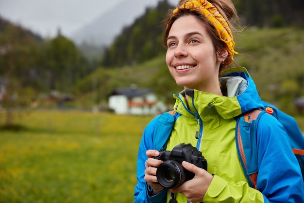 Image of pleasant looking cheerful woman dressed casually, holds professional camera