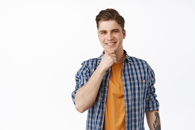 Image of pleased handsome guy, smiling man look thoughtful and touch chin, decide something, make interesting choice, intrigued with offer, white background