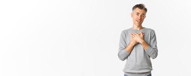 Free photo image of pleased and happy adult man with gray hair holding hands on heart and looking at something