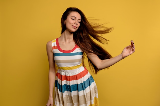 Image of a pretty smiling young woman in bright summer dress isolated over yellow wall. Fashion portrait of pretty girl posing having fun over colorful wall