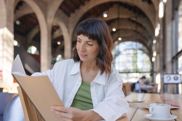 Immagine di una donna graziosa che tiene cartelle di lavoro nella caffetteria