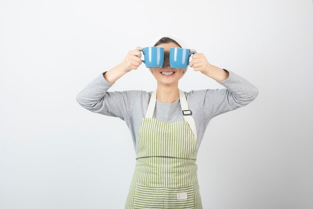 Image of a pretty young woman in apron covering eyes with two blue cups 