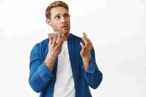 Free photo image of redhead man dictate voice message bending fingers as counting something during mobile conversation recording notes standing over white background copy space