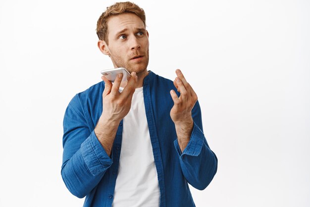 Image of redhead man dictate voice message bending fingers as counting something during mobile conversation recording notes standing over white background Copy space