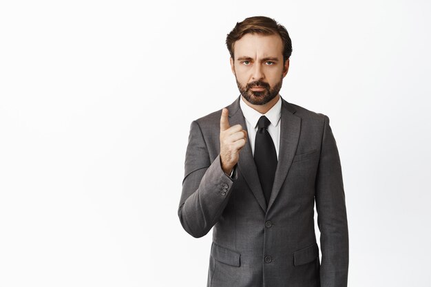 Image of serious boss scolding you businessman shaking finger furrow eyebrows taboo sign standing in suit over white background