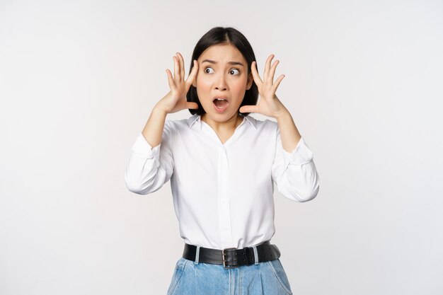 Image of shocked anxious asian woman in panic holding hands on head and worrying standing frustrated and scared against white background