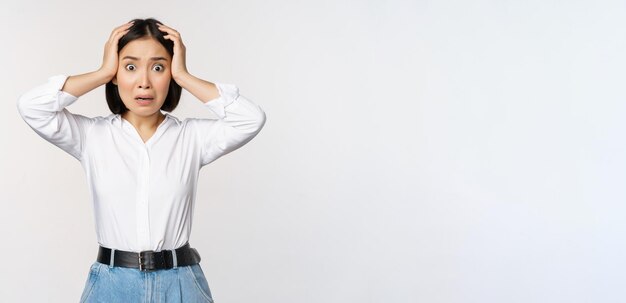 Image of shocked anxious asian woman in panic holding hands on head and worrying standing frustrated