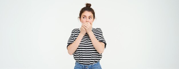 Image of shocked woman covers her mouth looks surprised stands over white background