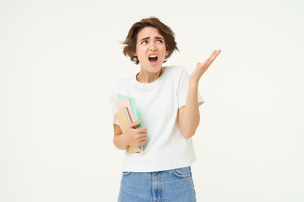 Image of shocked young woman holding notebooks shrugging and looking disappointed complaining at