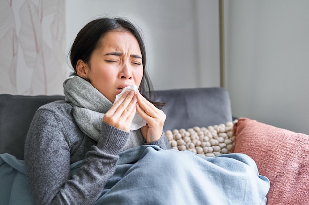 病気の韓国人女性が自宅で暖かい服とスカーフで覆われていて、風邪をひいて気分が悪くなっている画像
