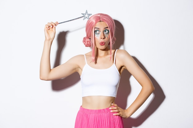 Image of silly attractive girl in pink wig, dressing as fairy for halloween party, hoding magic wand, standing.