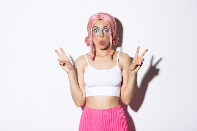 Image of silly girl in pink wig celebrating halloween showing funny faces and sticking tongue make p...