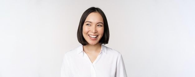 Image of smiling asian woman planning thinking of smth daydreaming standing over white background with smug face Copy space