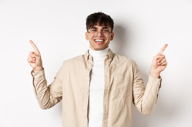 Free photo image of smiling handsome man in glasses pointing fingers sideways, showing advertisements or variants, standing cheerful on white background